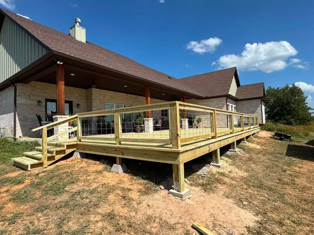 Finished 16 by 46 foot wood deck with cable railing behind the same brick home