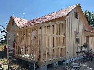 Home addition framed onto a board-and-batten house with a red metal roof